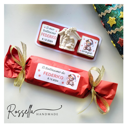 Bomboniera natalizia artigianale con cioccolatini personalizzati e calamita presepe, confezionata in carta rossa con nastro dorato a forma di caramella.